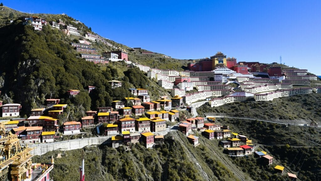 Colorful monastery buildings on a scenic hillside with clear blue skies, showcasing rural architecture.