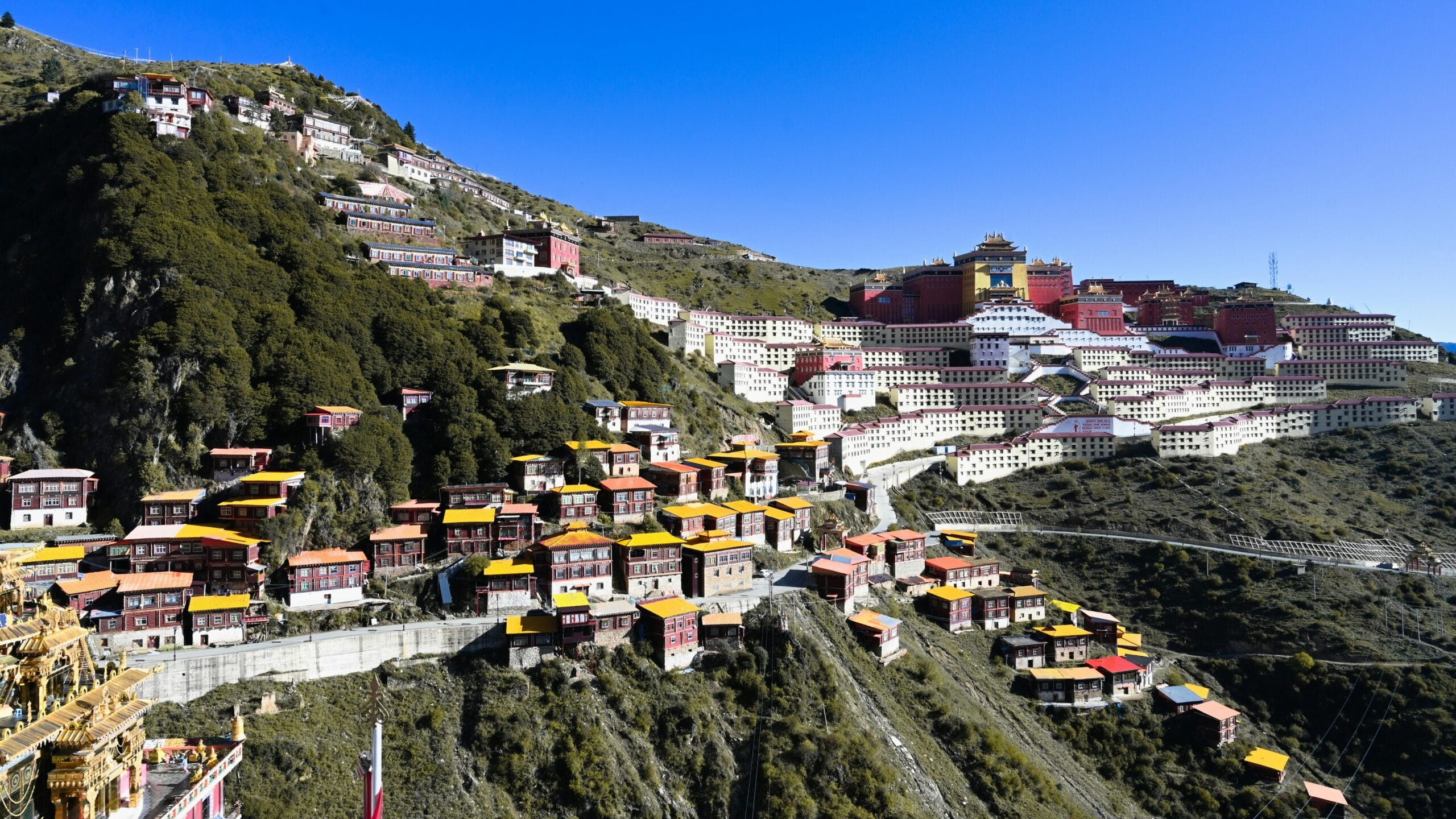 Colorful monastery buildings on a scenic hillside with clear blue skies, showcasing rural architecture.