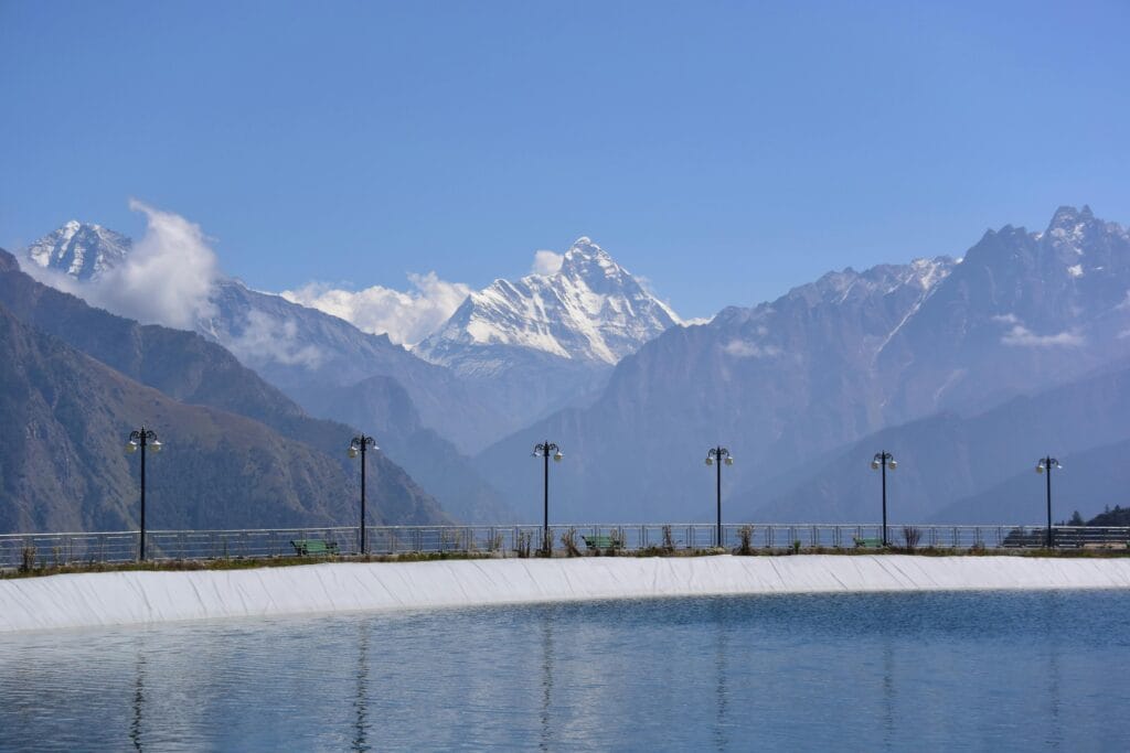 Scenic mountain landscape with snow peaks reflecting in a serene lake under a clear blue sky.
