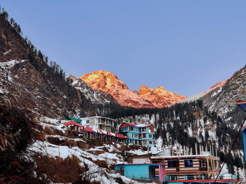 Picturesque village view with snow-capped mountains in Himachal Pradesh, India at sunrise.