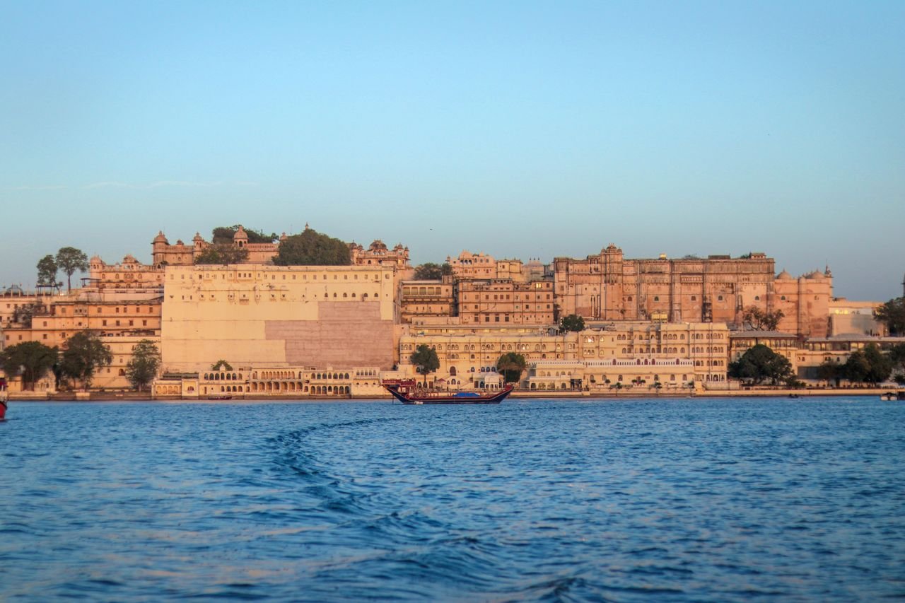View of the historic Udaipur City Palace in Rajasthan, India, across Lake Pichola during sunset.