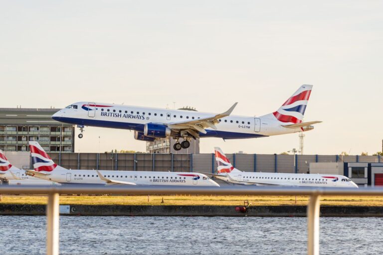 British Airways aircraft takes off, with others waiting, at a bustling airport during the day.